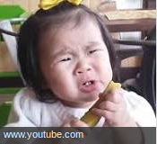 A young girl makes a sour face after taking a bite of a pickle
